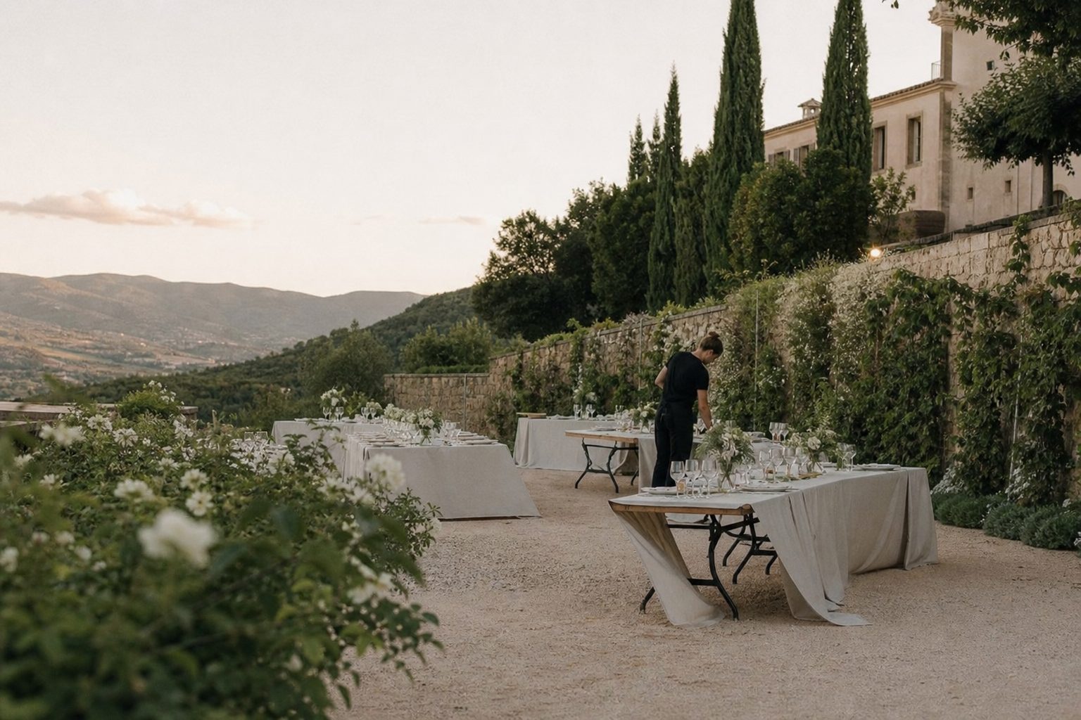 A vineyard terrace being set for a weekday reception, tables half dressed in ivory linen